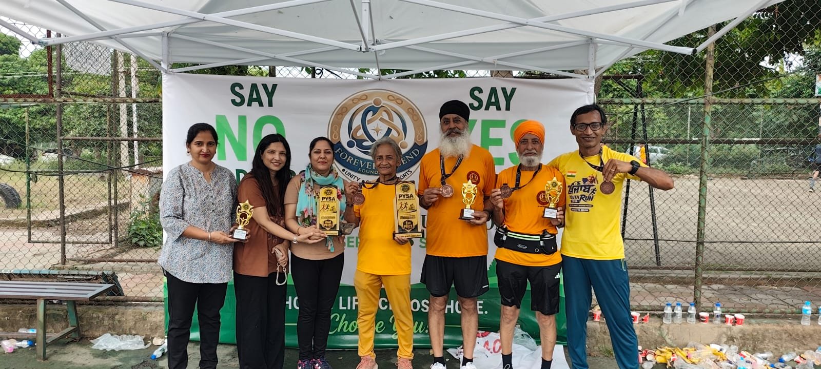 Participants and Forever Legend Foundation directors with trophies and medals in front of the Say No to Drugs, Say Yes to Life banner